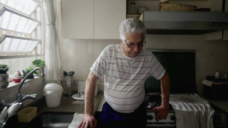 Foto de Hombre mayor preocupado de pie en la cocina casera rumiando pensamientos y recuerdos pasados sintiendo arrepentimiento y remordimiento - Imagen libre de derechos