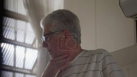 Téléchargez les photos : Anxieux vieil homme debout près de la fenêtre sentiment d'inquiétude. Regrettant cheveux gris personne couvant erreurs passées - en image libre de droit