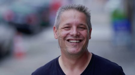 Photo for Joyful man smiling and laughing while standing in city street looking at camera. Portrait face close-up of a happy 40s person. Real life authentic people - Royalty Free Image
