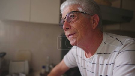 Foto de Hombre mayor en el momento de la esperanza, mirando hacia arriba hacia la ventana en casa, de pie en la cocina. Persona fiel - Imagen libre de derechos