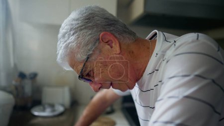 Photo for Mature man standing at kitchen counter struggling with old age and regret. Worried senior male person looking down frozen in brokeness - Royalty Free Image