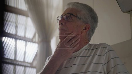 Photo for Anxious Older Man standing by window feeling worry. Regretful gray hair person brooding past mistakes - Royalty Free Image