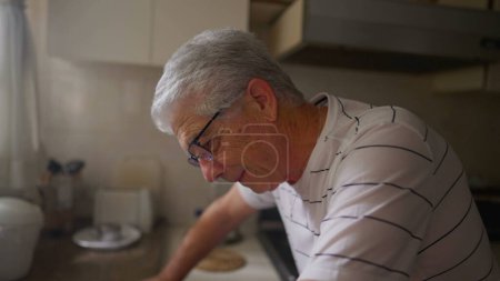 Photo for Worried senior man standing at kitchen counter leaning down by window feeling anxiety and suffering from difficulties and regret - Royalty Free Image