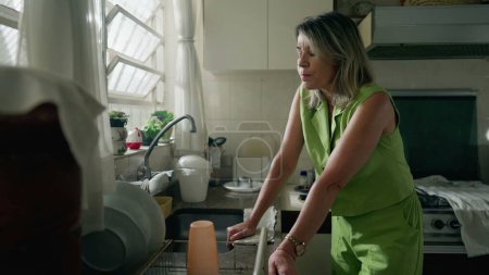Téléchargez les photos : Habitation dans la détresse, femme d'âge moyen éprouvant l'anxiété dans la cuisine - en image libre de droit