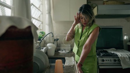 Foto de Una mujer ansiosa de mediana edad de pie en la cocina sufriendo de estrés y angustia. Una mujer caucásica en los años 50 sintiendo pesar y ansiedad - Imagen libre de derechos