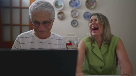 Téléchargez les photos : Joyeux couple d'âge mûr rire ensemble tout en utilisant un ordinateur portable - en image libre de droit