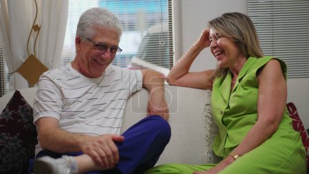 Photo for Happy mature man and woman conversing seated on couch at home indoors. Senior man and middle-aged female caucasian woman interacting, smiling and laughing together - Royalty Free Image