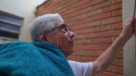 Photo for Elderly Man putting towels on shoulder after removing them from clothelines, doing domestic household chores activities - Royalty Free Image