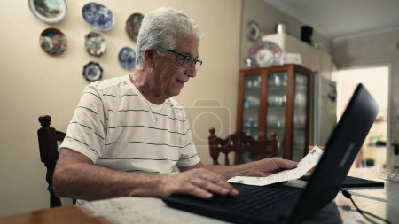 Photo for Senior Citizen Concerned Over Fine Debt Paper Beside Laptop, troubled retired man using computer to pay due bill - Royalty Free Image