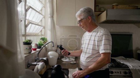 Foto de Hombre mayor feliz reacción a la notificación de buenas noticias del dispositivo de teléfono móvil mientras está de pie en la cocina - Imagen libre de derechos