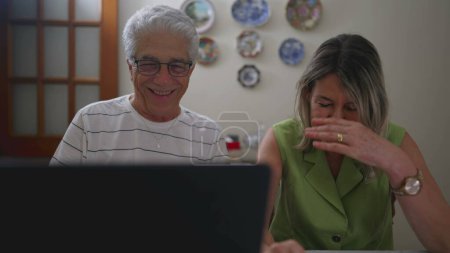 Téléchargez les photos : Joyeux couple d'âge mûr rire ensemble tout en utilisant un ordinateur portable - en image libre de droit