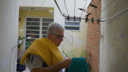 Photo for Older man removing towels from drying hangers in home backyard, elderly person doing household chore activities, casual domestic lifestyle scene in old age - Royalty Free Image