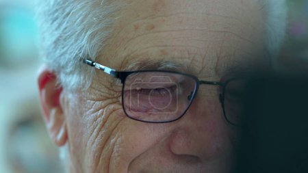 Photo for Close-up of an elderly man face staring at computer screen off camera. Older person in 70s wearing reading glasses browsing internet - Royalty Free Image