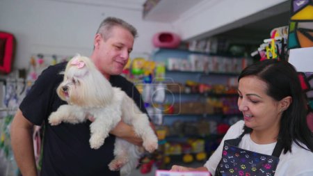Téléchargez les photos : Propriétaire d'un animalerie remettant un petit chien au client après avoir toiletté un animal de compagnie dans un magasin d'affaires local - en image libre de droit