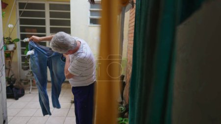 Photo for Senior man reverting pants from the inside out after drying on hanger, older person doing domestic chore routine by straightening jeans - Royalty Free Image