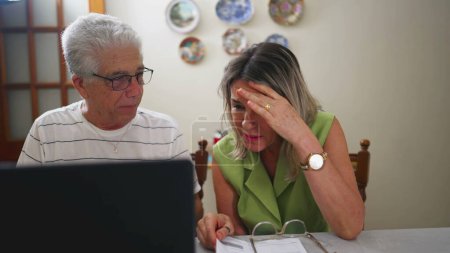 Téléchargez les photos : Couple de personnes âgées en difficulté faisant face à des problèmes financiers devant un ordinateur portable dans la cuisine - en image libre de droit