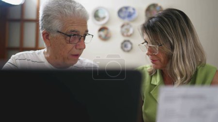 Téléchargez les photos : Couple âgé stressé examinant les finances, étudiant le document dans la cuisine de la maison - en image libre de droit