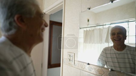 Téléchargez les photos : Heureux homme âgé regardant sa propre salle de bain reflet souriant, personne âgée commençant la journée avec une disposition positive - en image libre de droit