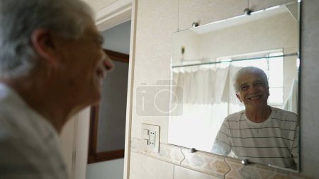Happy senior man staring at his own bathroom reflection smiling, older person starting the day with positive disposition
