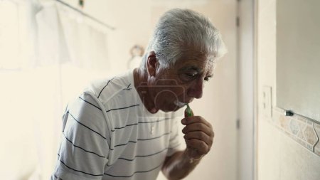 Photo for Senior morning routine brushing in mirror while staring at his own reflection in bathroom miror. Dental hygiene, elderly person starting the day - Royalty Free Image