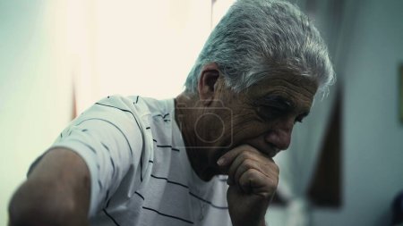 Foto de Hombre mayor pensativo deprimido con pelo gris en profunda reflexión mental sentado en habitación sombría con atmósfera oscura y malhumorada - Imagen libre de derechos
