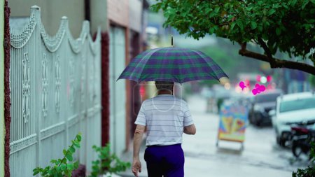 Téléchargez les photos : Un homme plus âgé sort sous la pluie, ouvre un parapluie et ferme la porte, marche sur le trottoir - en image libre de droit