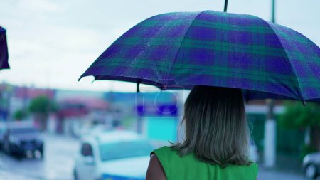 Téléchargez les photos : Dos de femme tenant parapluie marchant dans la rue sous la pluie - en image libre de droit