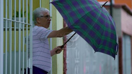 Téléchargez les photos : Un aîné ouvre son parapluie, sort dans la rue sous la pluie, ferme la porte de la maison derrière lui. Personne âgée quittant la résidence pendant la journée de pluie au ralenti - en image libre de droit