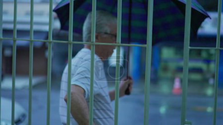 Téléchargez les photos : Un aîné sort dans la rue pendant la soirée pluvieuse, ouvre son parapluie et marche sur le trottoir au ralenti. Personnes âgées quittant la résidence, fermeture de la porte - en image libre de droit