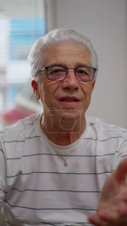 Photo for Senior man talking to webcam participating in video-conference speaking with family relatives using modern tech, Video call with grandfather, in Vertical Video - Royalty Free Image