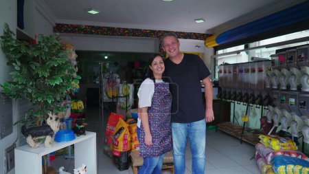 Téléchargez les photos : Propriétaires de petite entreprise de Animalerie brésilienne debout à l'intérieur du magasin souriant à la caméra, couple marié mari et femme partenaires - en image libre de droit