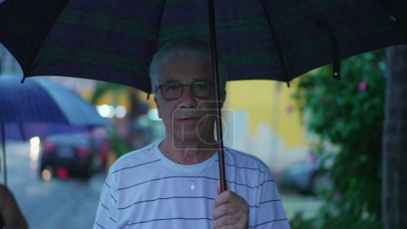 Téléchargez les photos : Homme mûr se promener sur le trottoir urbain, tenant parapluie dans l'après-midi pluvieux - en image libre de droit