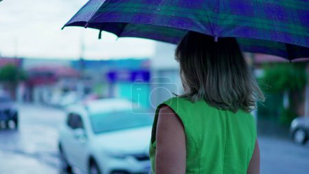 Téléchargez les photos : Dos de femme tenant parapluie marchant dans la rue sous la pluie - en image libre de droit