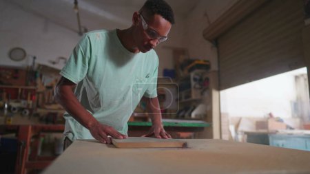 Photo for One young black carpenter using machine to trim piece of wood at workshop. Focused employee of carpentry business working meticulously - Royalty Free Image