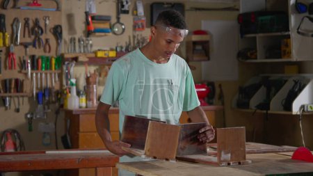 Téléchargez les photos : Un jeune apprenti noir travaillant à l'atelier de menuiserie. Artisanat emploi occupation bâtiment meubles - en image libre de droit