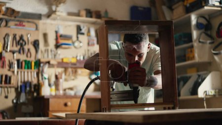 Téléchargez les photos : Jeune menuisier noir Meubles d'artisanat dans l'atelier de menuiserie en utilisant un équipement de forage - en image libre de droit