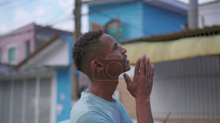 Téléchargez les photos : Un religieux noir sud-américain priant Dieu alors qu'il se tenait dans la rue urbaine. Une personne brésilienne fidèle et pleine d'espoir qui regarde vers le haut vers l'aide et le soutien divins - en image libre de droit
