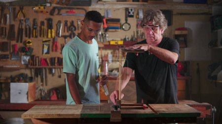 Foto de Carpintero trabajando en el taller con la ayuda de aprendiz, trabajador de la pequeña empresa haciendo carpintería en el lugar de trabajo de carpintería - Imagen libre de derechos