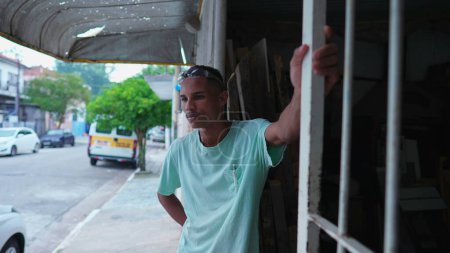 Téléchargez les photos : Charpentier brésilien réfléchi prenant une pause du travail, debout devant un magasin local - en image libre de droit