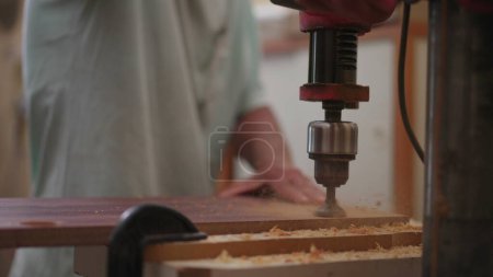 Photo for Drilling a hole into wooden surface with the use of an industrial machine in slow-motion. Hand handling carpentry equipment at workshop, detail close-up - Royalty Free Image