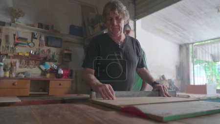 Téléchargez les photos : Maître charpentier travaillant dans un atelier de menuiserie, tranchant du bois avec une scie. Artisanat artisanal au magasin local, atelier de bois - en image libre de droit