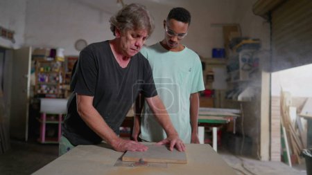 Foto de Maestro carpintero orientando aprendiz para trabajar con máquina en taller de carpintería de carpintería. Joven empleado observando proceso de artesanía - Imagen libre de derechos