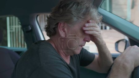 Photo for Old man experiencing sadness holding on into car's steering wheel parked on street sidewalk. Desperate senior person suffering from depression struggling with daily activities - Royalty Free Image