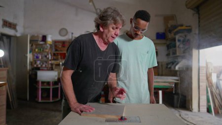 Photo for Master carpenter orienting apprentice to work with machine at woodworking carpentry workshop. Young employee observing craftsmanship process - Royalty Free Image