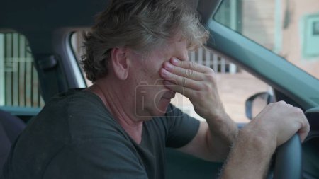 Photo for Old man experiencing sadness holding on into car's steering wheel parked on street sidewalk. Desperate senior person suffering from depression struggling with daily activities - Royalty Free Image