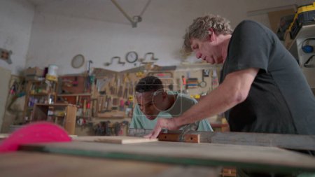 Téléchargez les photos : Maître charpentier guidant l'élève apprenti à l'atelier de menuiserie, processus de profession d'emploi. Senior homme enseignant étudiant - en image libre de droit