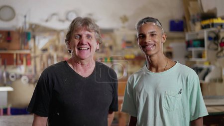 Foto de Retrato de carpinteros mayores y aprendices de pie dentro de un taller de madera sonriendo a la cámara - Imagen libre de derechos