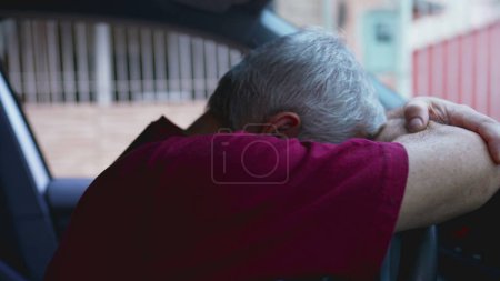 Téléchargez les photos : Homme âgé seul souffrant, assis à l'intérieur de la voiture garée appuyé sur le volant de la voiture dans le désespoir calme. Lutte anxieuse personne âgée se sentant désespoir émotionnel - en image libre de droit