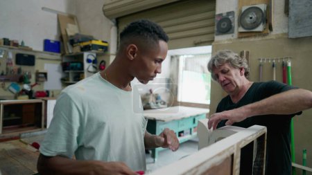 Téléchargez les photos : Menuisiers travaillant à l'atelier. Senior et jeune employé polissage de meubles en bois, authentique petite entreprise brésilienne en Amérique du Sud - en image libre de droit