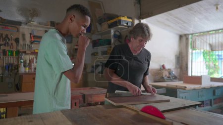 Téléchargez les photos : Mentor charpentier enseignant Apprenti scie opération de la machine dans l'atelier - en image libre de droit